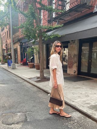 Robin Reetz in New York City wearing a silk slip, oversized white button-down shirt, minimalist flip-flops, Thistles eyewear, and carrying a Jil Sander bag.