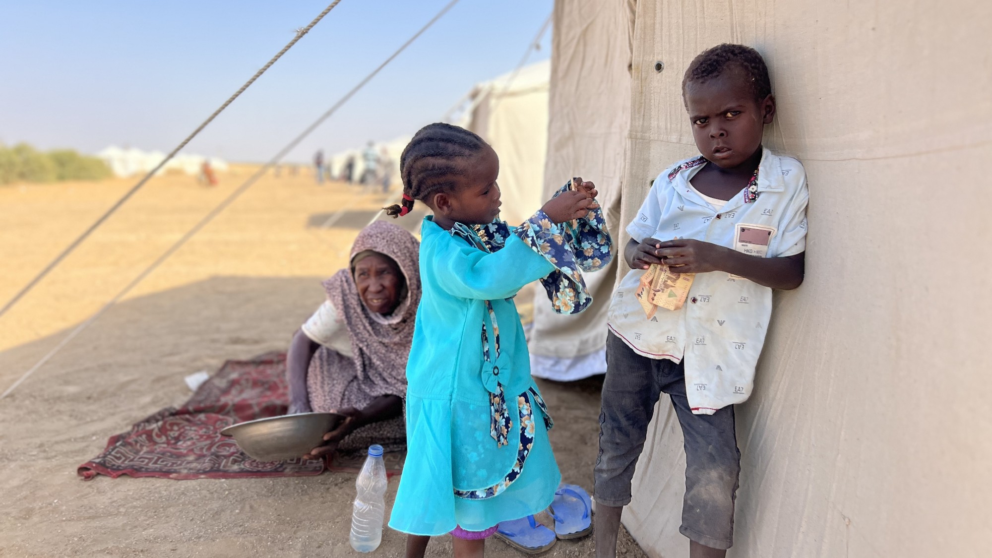 A woman and two children sit outside a tent at the Al-Afadh refugee camp in Al Dabbah, Sudan