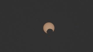 photo of the yellow-orange sun being partially eclipse by the potato-shaped mars moon phobos