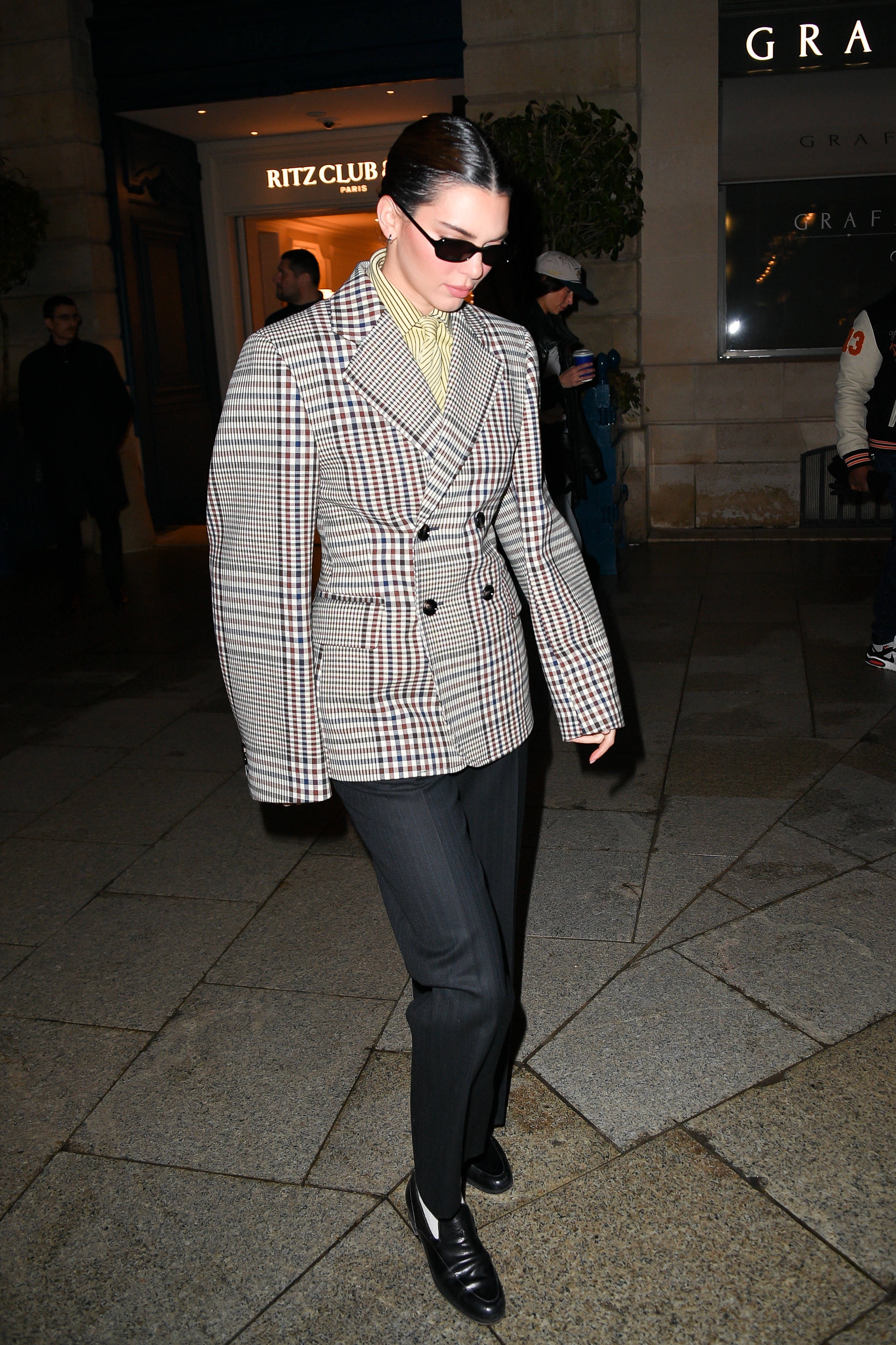 Kendall Jenner in Paris during Paris Fashion Week wearing a Bottega Veneta checkered jacket, jacquard striped shirt and tie, and wool trousers.