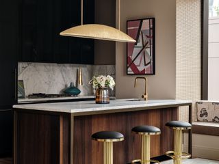 A kitchen with gold accents and bar stools around an peninsular island