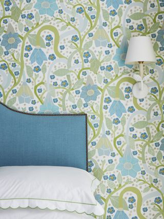 A bedroom with an aqua headboard, blue-toned wallapaper and white sheets
