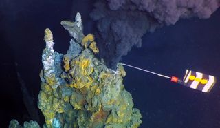 black, mineral-filled water shown spewing out of a hydrothermal vent that a robot is collecting samples from