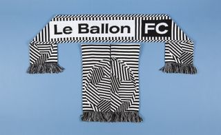 A black and white zebra scarf on top and two folded scarfs below. The scarf has an embroidered white patch with black text "Le Ballon" followed by a black patch and white text "FC".