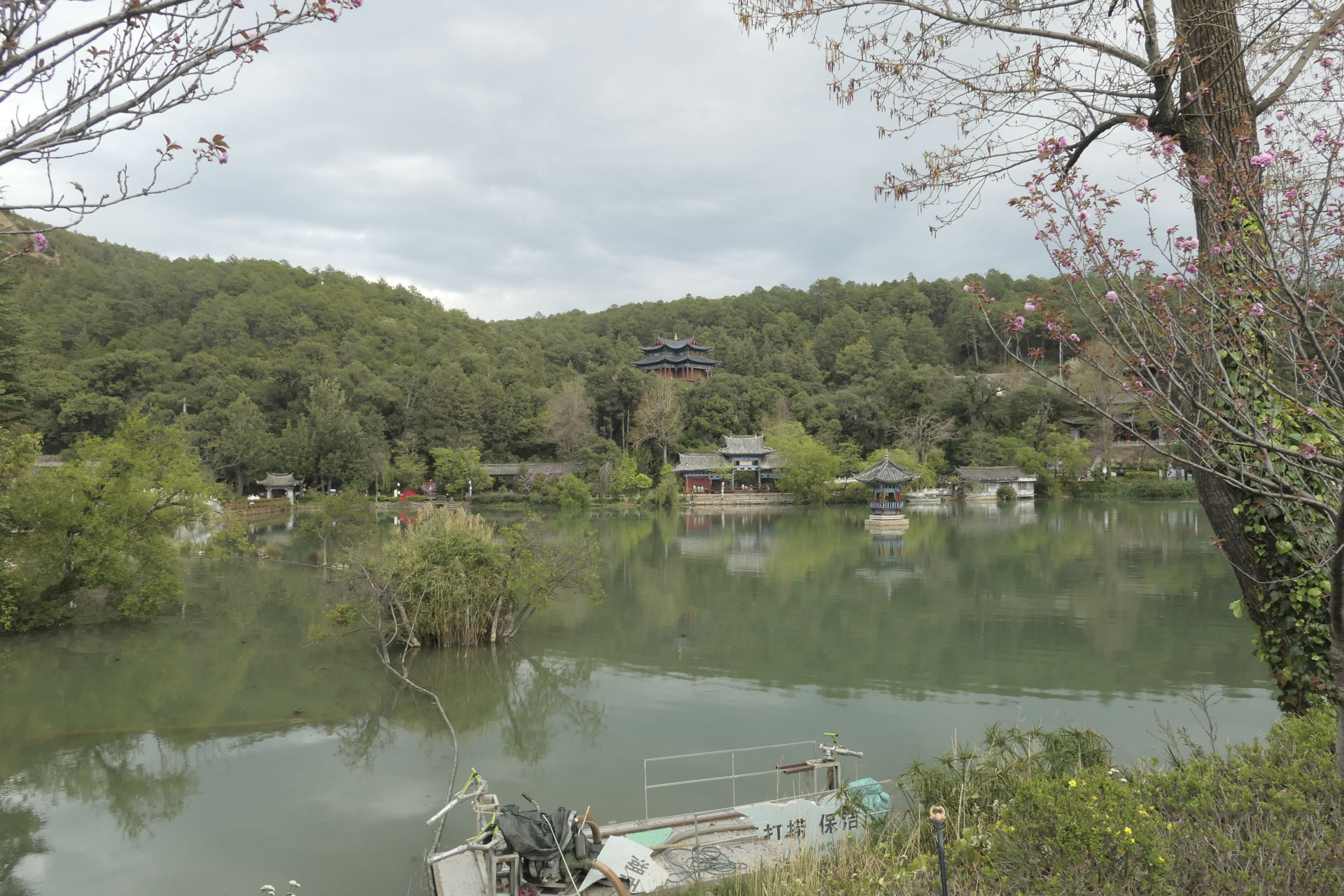 A Chinese temple nestled among trees, with a still lake in the foreground