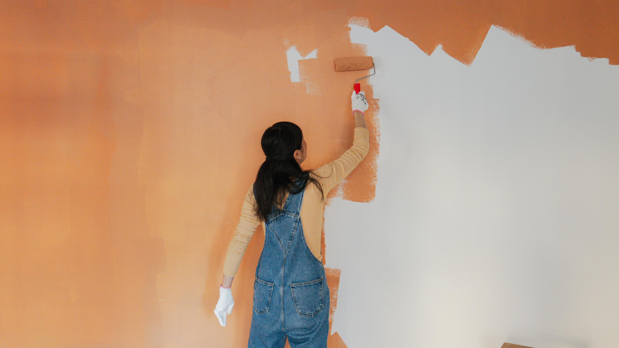 back of a person painting a wall orange