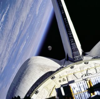 The space shuttle Discovery in orbit with the moon