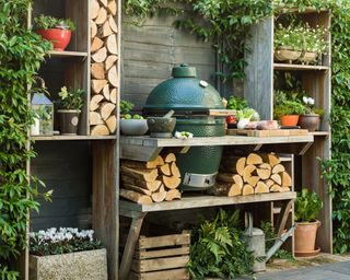 A green barbecue in a rustic wooden and log-filled outdoor kitchen space.