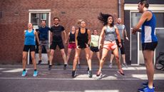 Group of runners jumping, while one runner stands looking on timing them with a watch