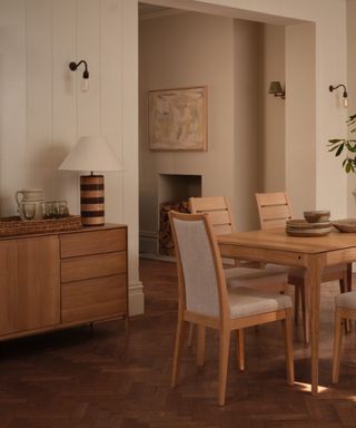 A neutrally painted dining room with a wooden table and six chairs, and a matching wooden sideboard with a lamp on top.