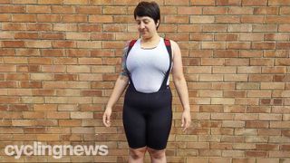 The Castelli Premio Black Bib Shorts worn over a white sleeveless base layer, modelled by a chubby tattooed woman with short dark hair, standing in front of a wall