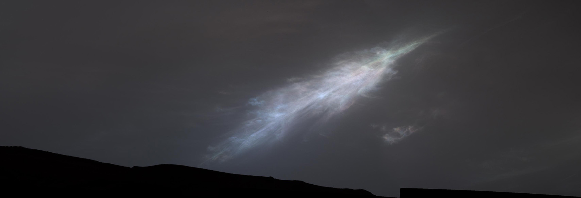 A glowing white light in a dark night sky with a silhouetted landscape below.