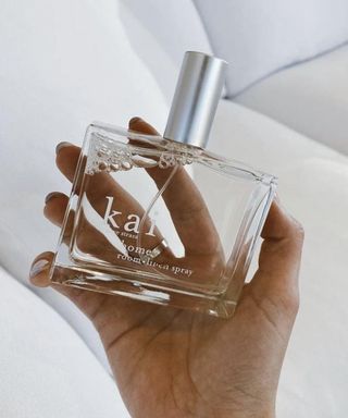 A person with white nail polish holding a bottle of Kai room linen spray