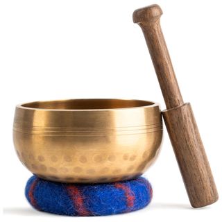 A gold sound bowl next to a wooden stick on a blue and red felt rest