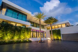 A modern double storey white house with palm trees and shrubbery around it.