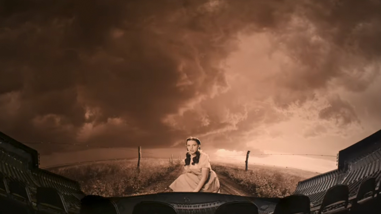 A black and white scene from The Wizard of Oz with Dorothy in the middle, on the screen at Sphere with seats in the foreground.
