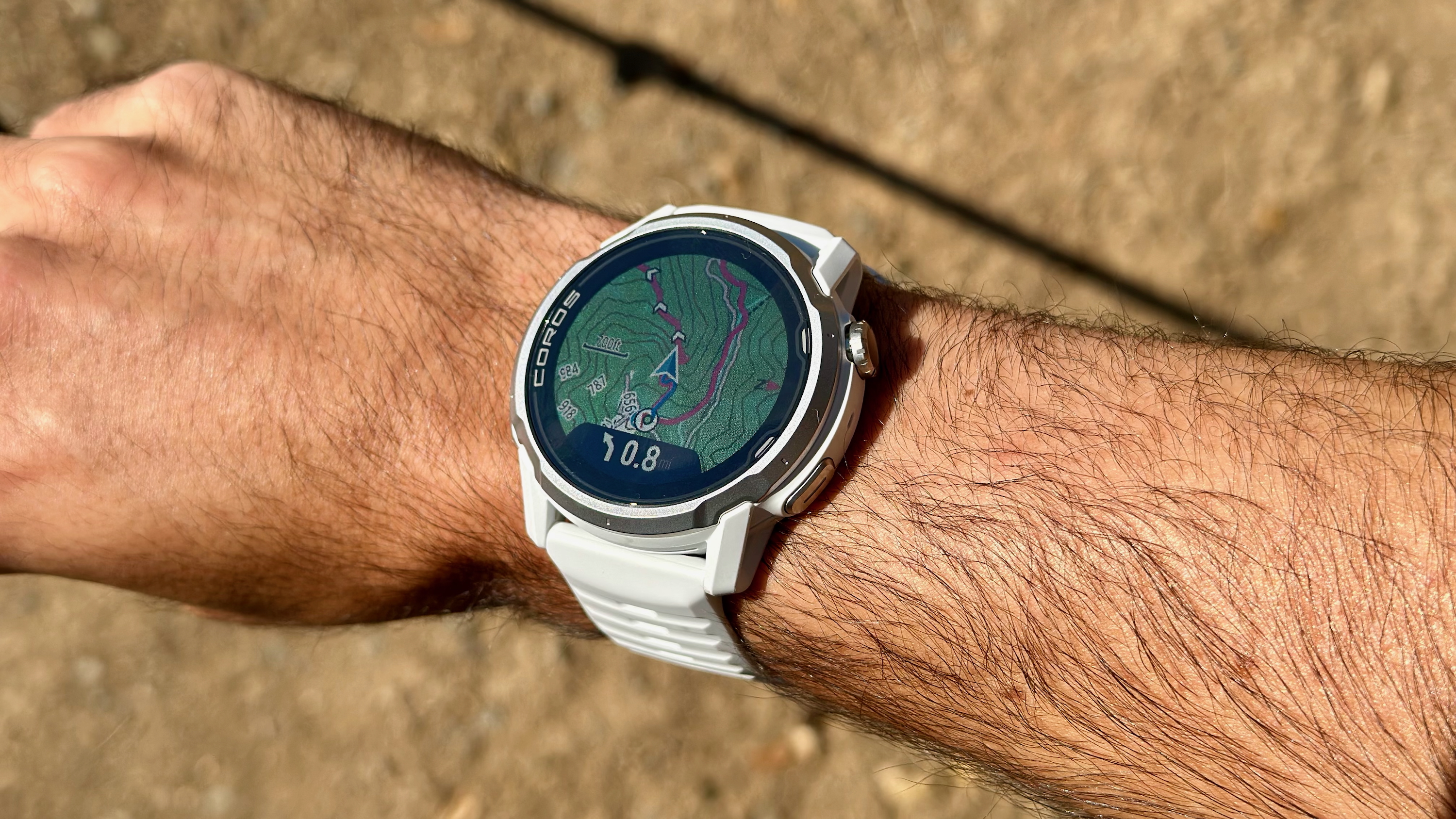 A photo of the COROS APEX 4 on the author's wrist showing a topographic map with turn-by-turn navigation and a course line.