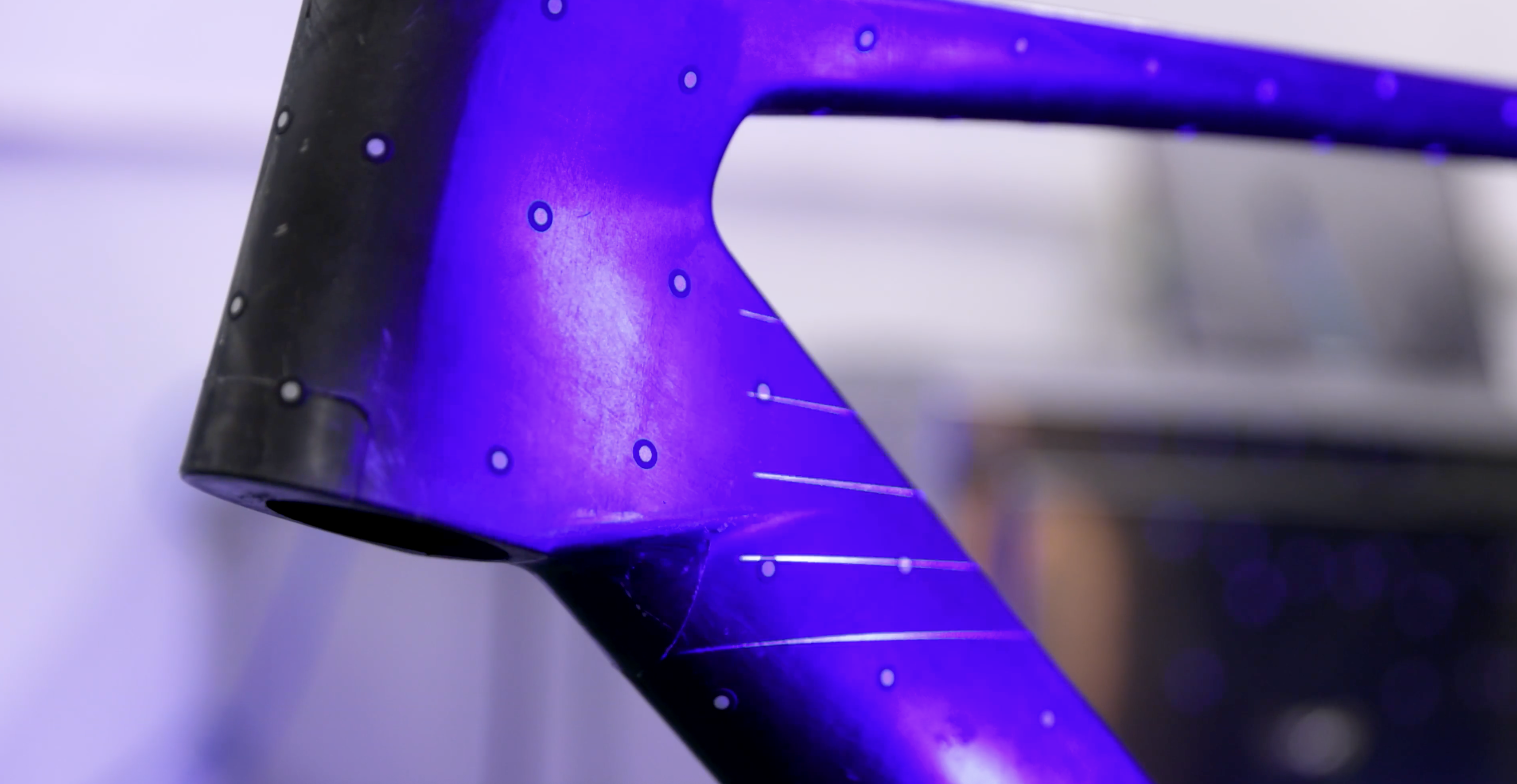 A carbon bike frame with dots on it lit purple by a laser