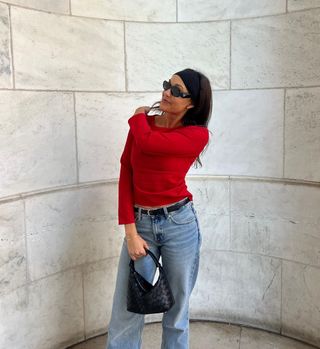 @annadzhenderson wearing red top, blue jeans, and black accessories