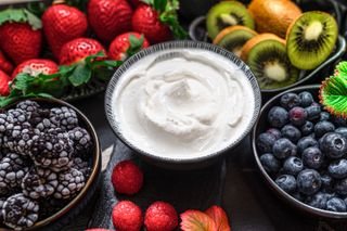A bowl of yogurt surrounded by bowls of fruit
