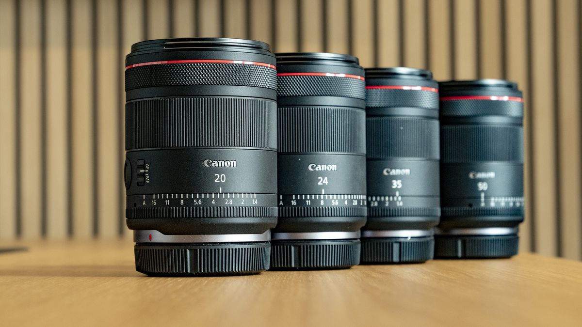 Canon RF 20mm F1.4L VCM lens on a wooden table, alongside three other Canon hybrid prime lenses