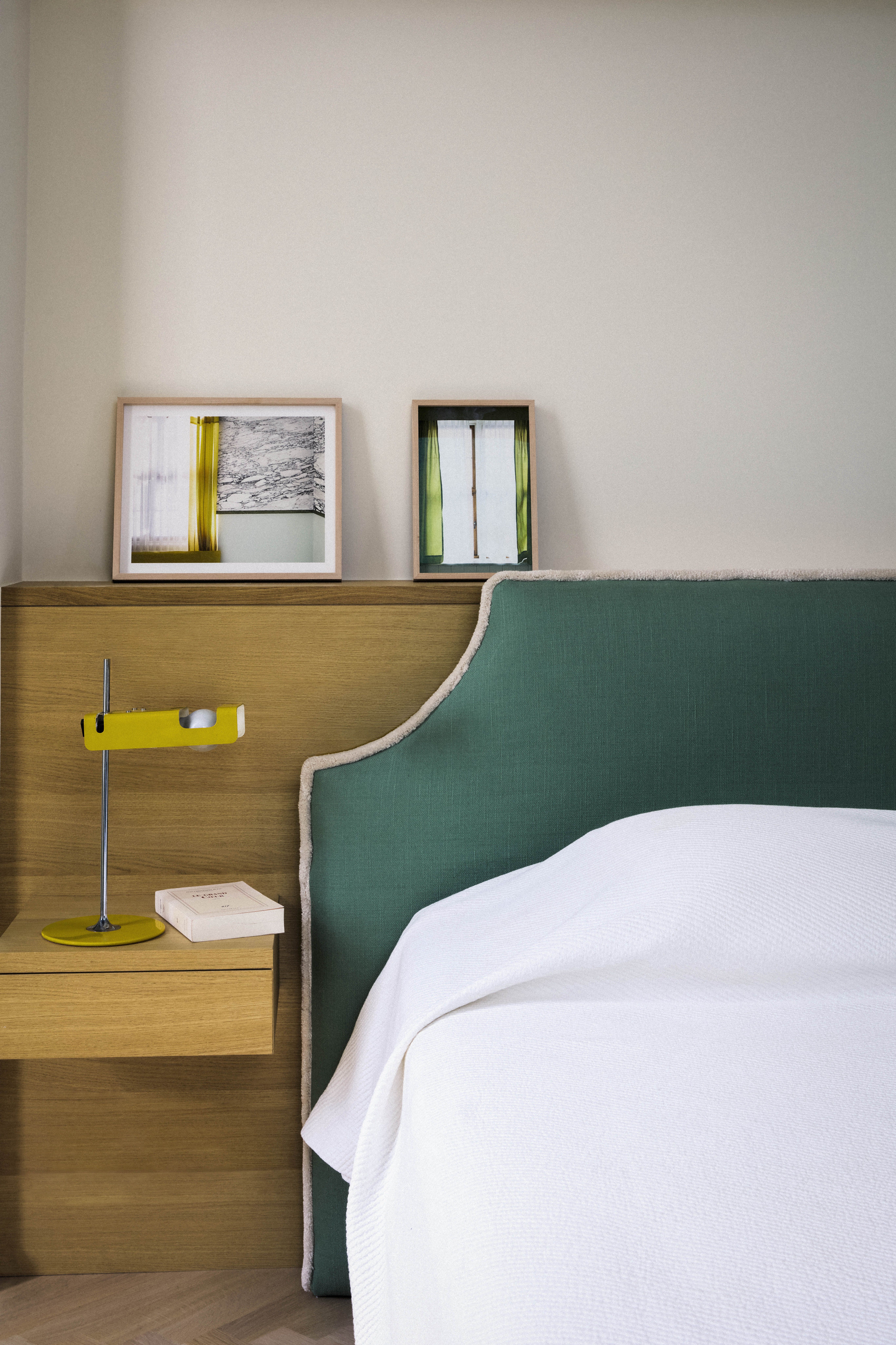 A bedroom in green tones, with a velvet headboard, printed green curtains and wooden flooring