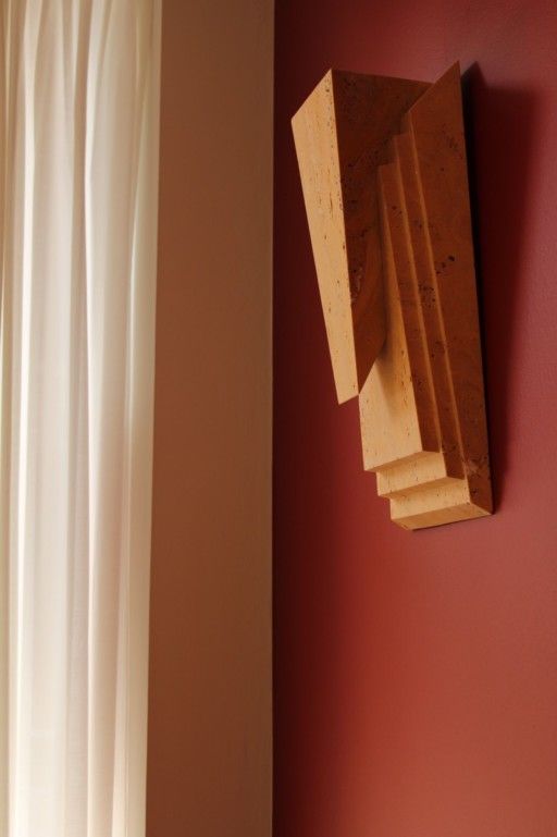 A wooden sculpture hangs on a red wall next to a white curtain.
