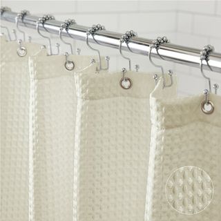 A cream waffle shower curtain hanging from a silver curtain pole. 