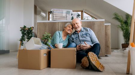 A senior couple sitting on the floor with boxes after downsizing in retirement.