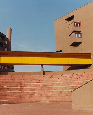 A pink arena-like with staircases in an open space. Above is a raised yellow walkways which connect the blocks to each other,
