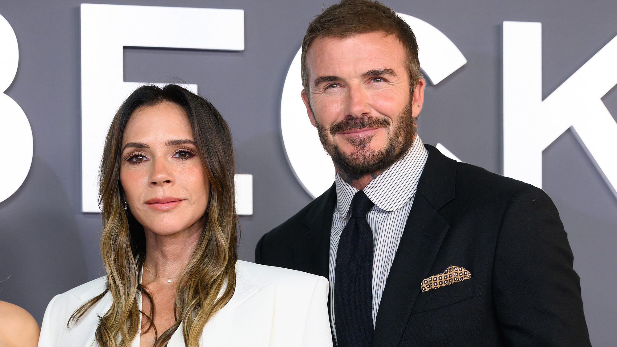 Victoria Beckham and David Beckham in front of a grey background with white lettering. The couple is attending the &quot;Victoria Beckham&quot; World Premiere.