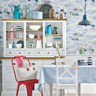 A dining room with coastal wallpaper and white wooden dresser storage