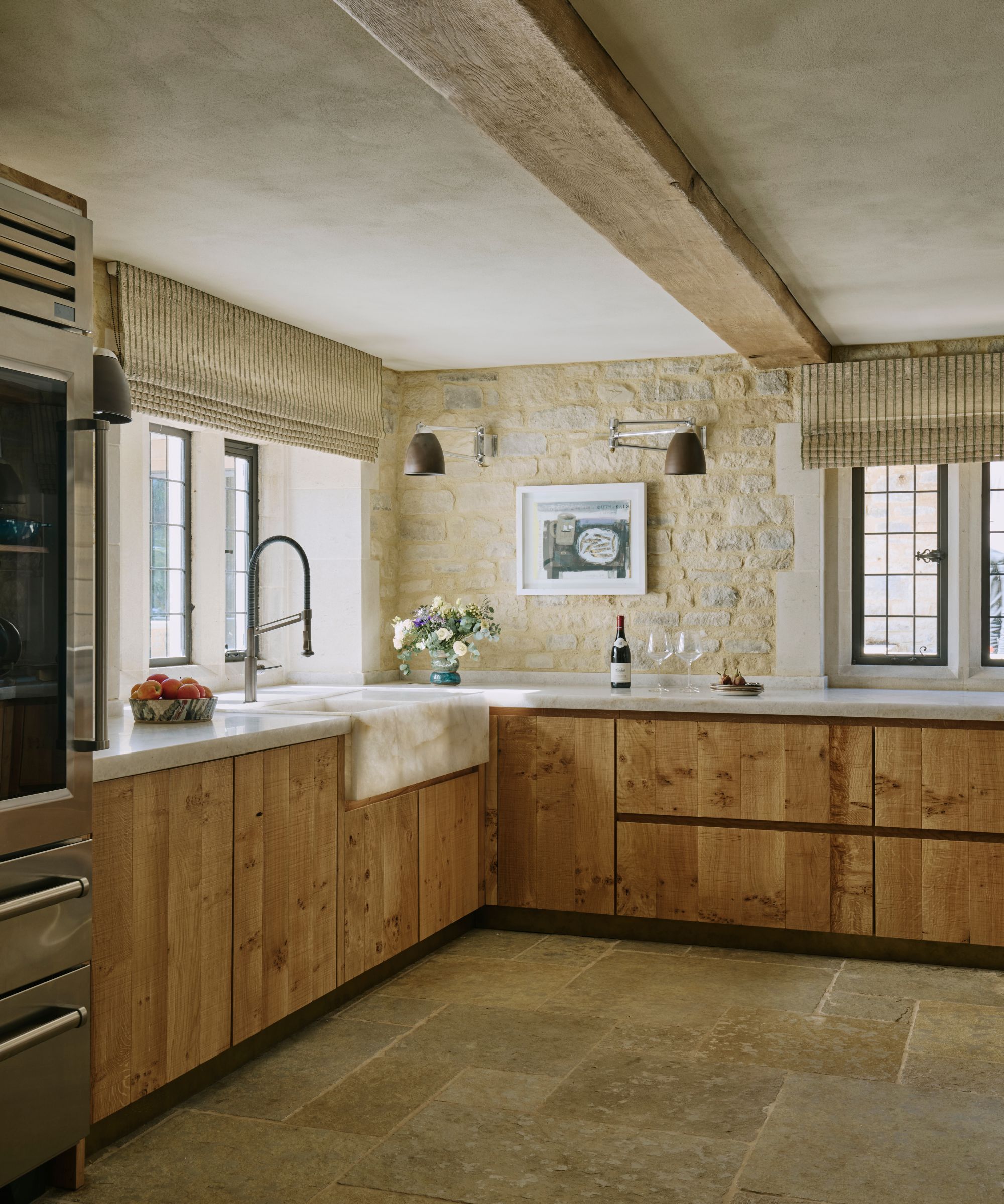 A Cotswolds kitchen with wood cabinets, marble countertops, stone flooring and exposed stone walls