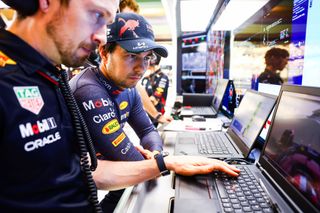 F1 driver Sergio Perez of Mexico and Oracle Red Bull Racing, sat with his team in the pit looking at data on laptops.