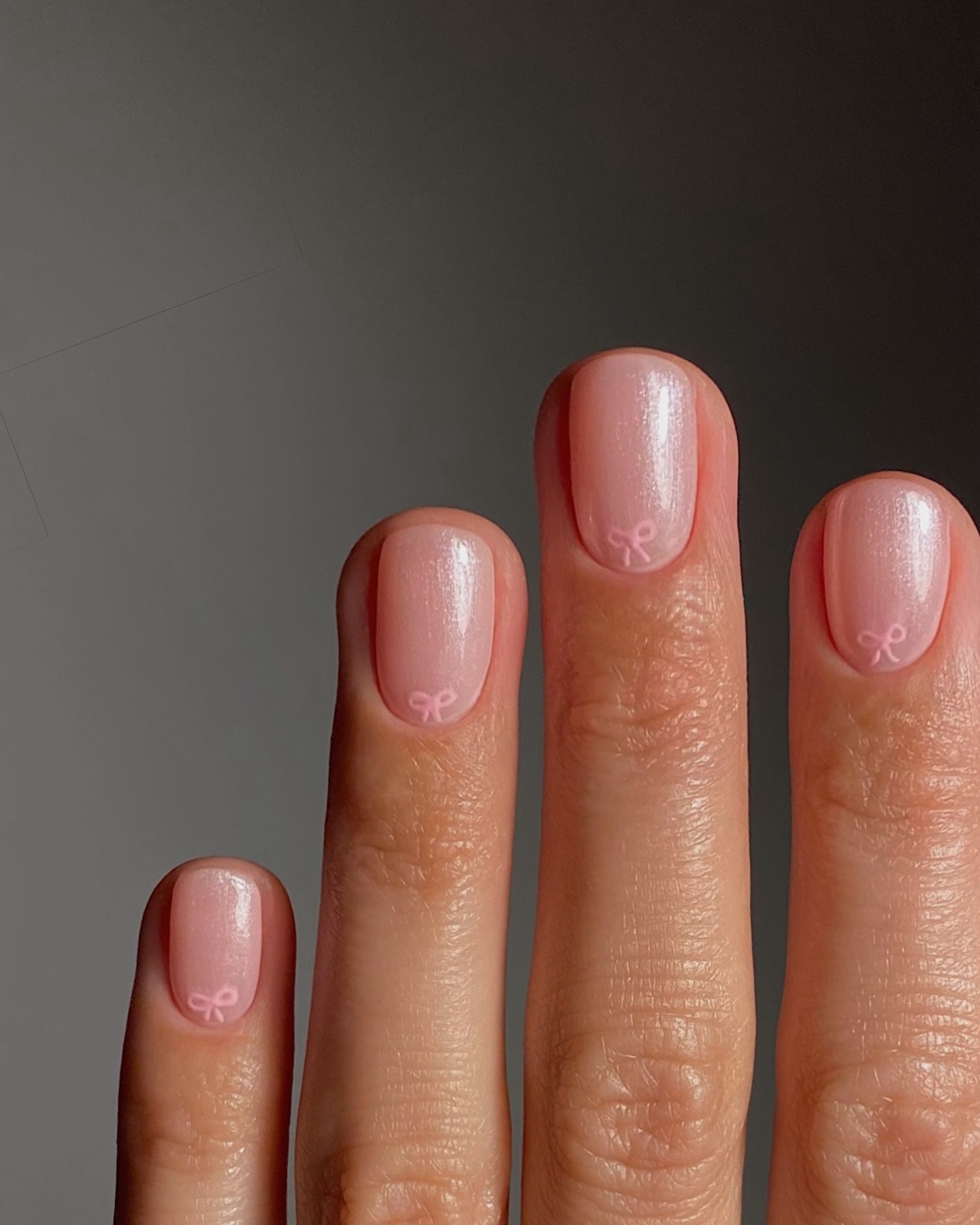 A close-up picture of a chrome manicure with baby pink bows