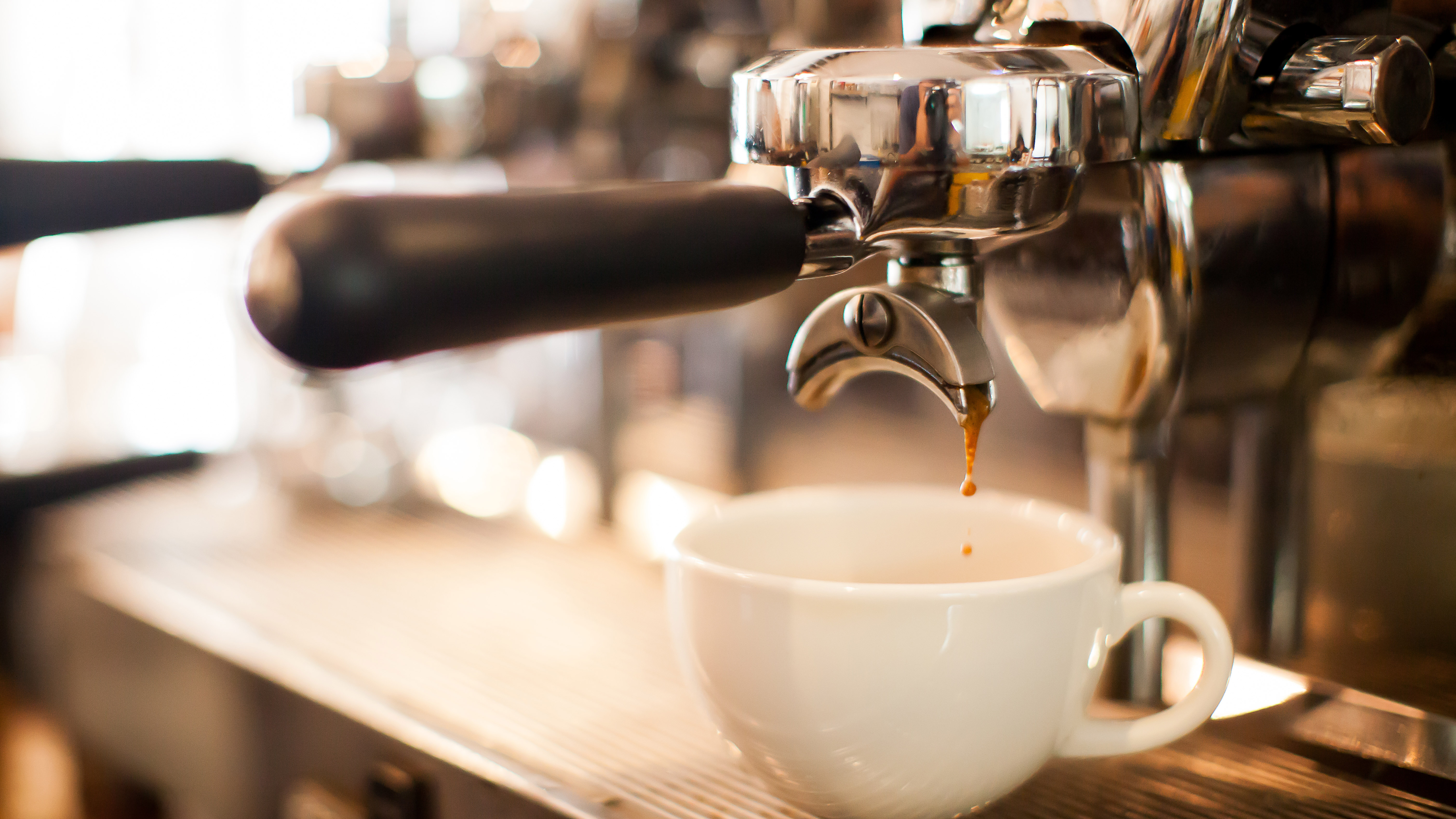 A coffee cup on a espresso machine and coffee starting to brew