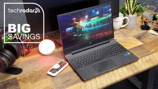 The HP Victus 15 on a desk during our review, with a white TechRadar badge that reads 'Big Savings' in the upper left corner