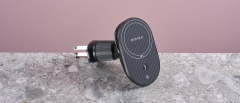 The Pitaka MagEZ Car Mount Pro 2 Qi2 sits on a stone-effect surface with a pink background. The view is of the front profile at a slight angle, revealing the collar fasteners and the metal attachment hooks.