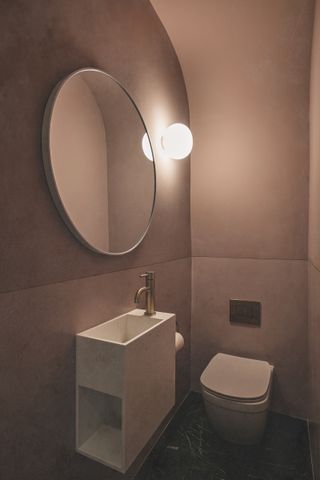 A small powder room painted in a dusty pink with a round mirror