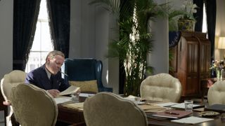 Kiefer Sutherland as Franklin D Roosevelt in The First Lady sitting at a table smoking and wearing glasses and a navy pinstripe suit
