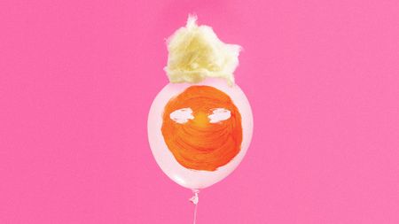 Photo collage of a pink balloon with orange pain splash on it, and a tuft of yellow spun sugar on the top.