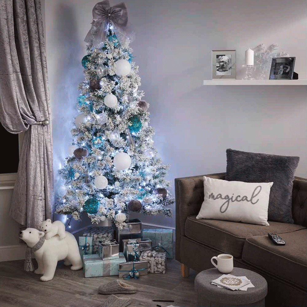 A white Christmas tree decorated with white lights and a large bow on top in a coy white living room