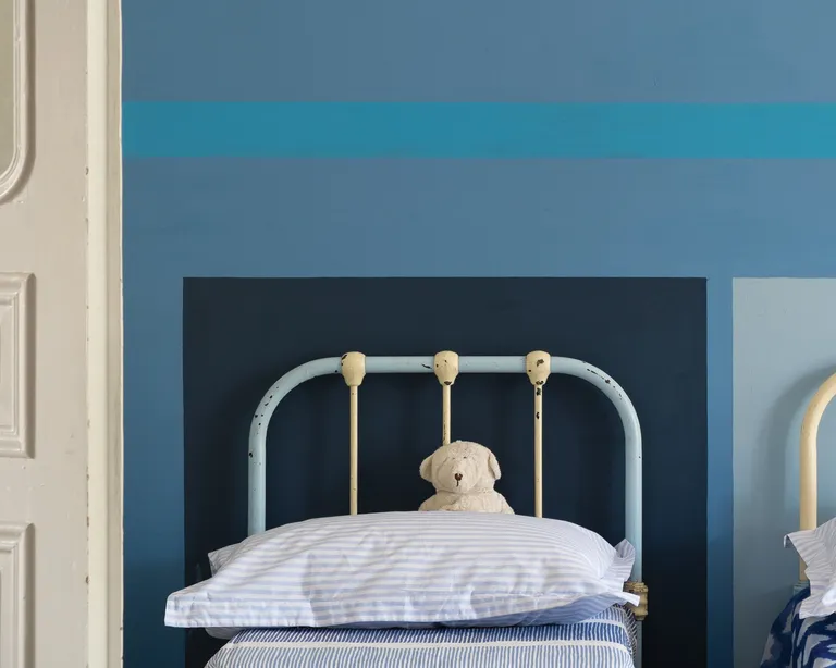 A kids' bedroom with twin beds and blue walls painted in a graphic design in differing tones