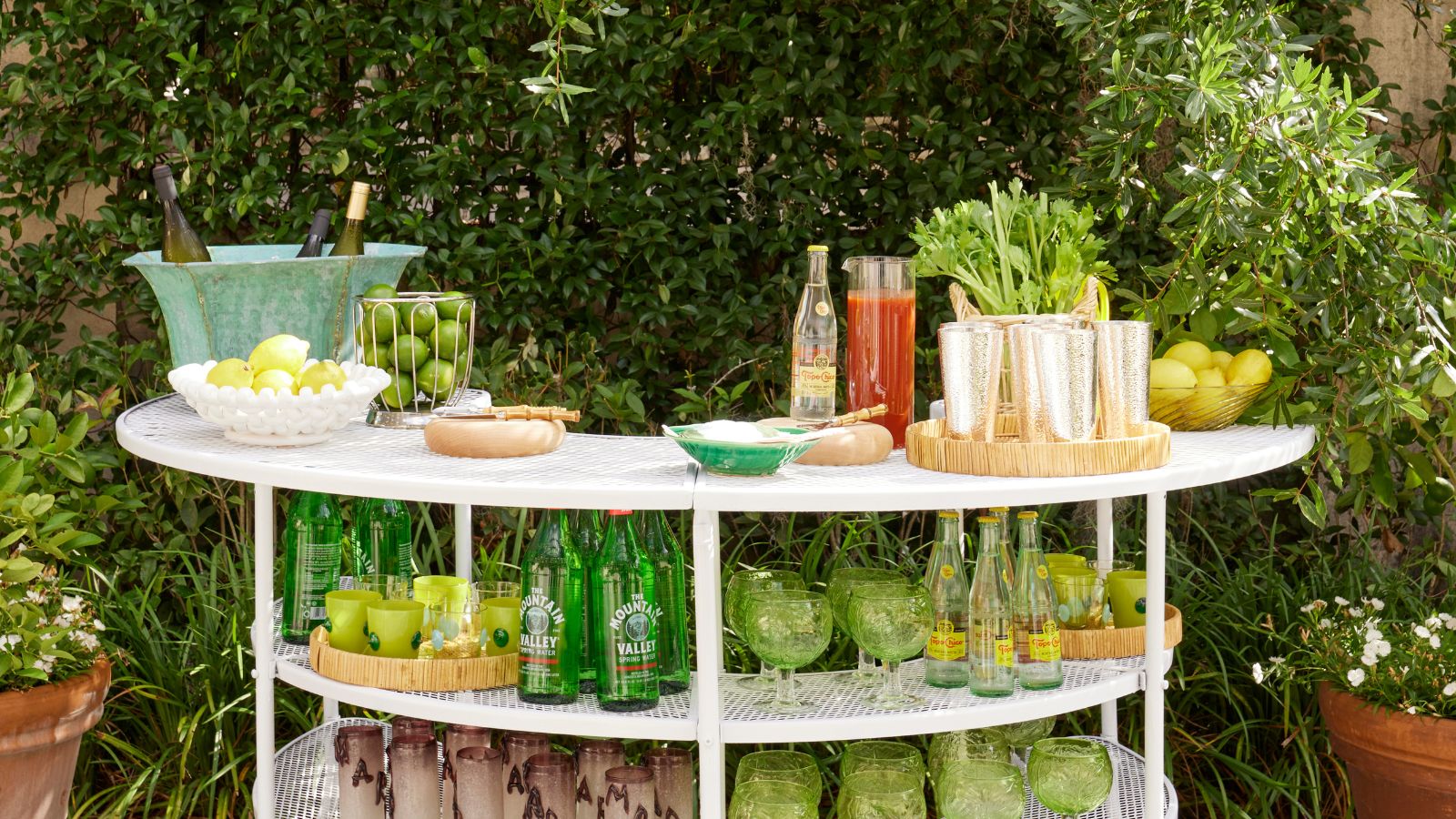 Outdoor drinks station with green glassware, rattan trays and fruit bowls