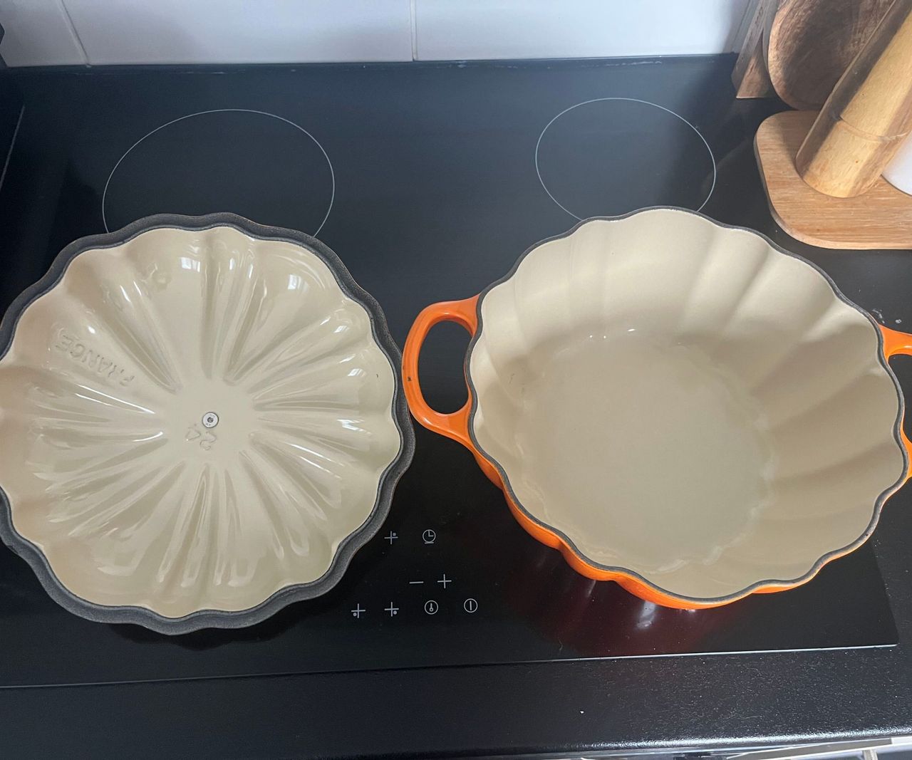 An orange Le Creuset pumpkin Cocotte on a black kitchen stove top