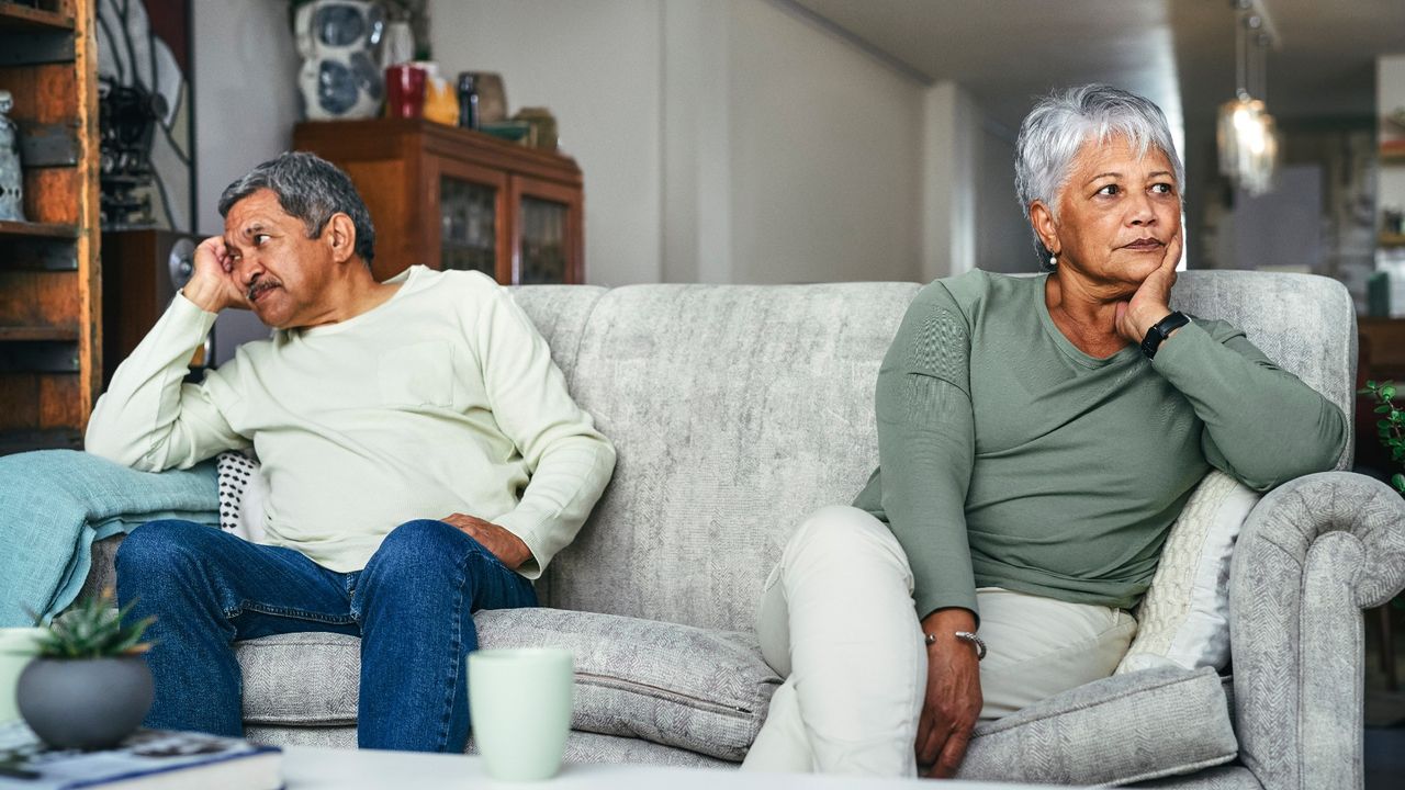 A senior couple sitting on opposite sides of the couch, having a disagreement