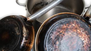 The scorched underside of two stainless steel pans with a third pan behind