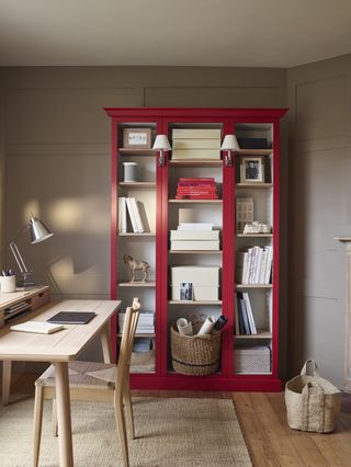 stone home office with red painted cabinet, blonde wood desk and chair, coir rug, wooden floor, basket, chrome desk lamp