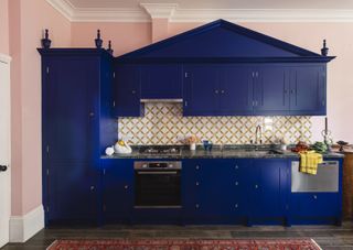 A single galley kitchen with blue cabinets and mosaic tiles in front of a pink wall