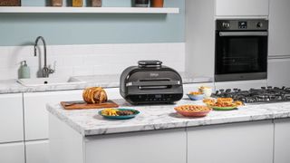 The Ninja Smart XL Grill and Air Fryer on a kitchen island surrounded by food